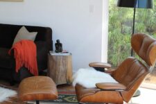 a mid-century modern living room with a black sofa, an amber leather chair with an ottoman, a black floor lamp and a bold rug