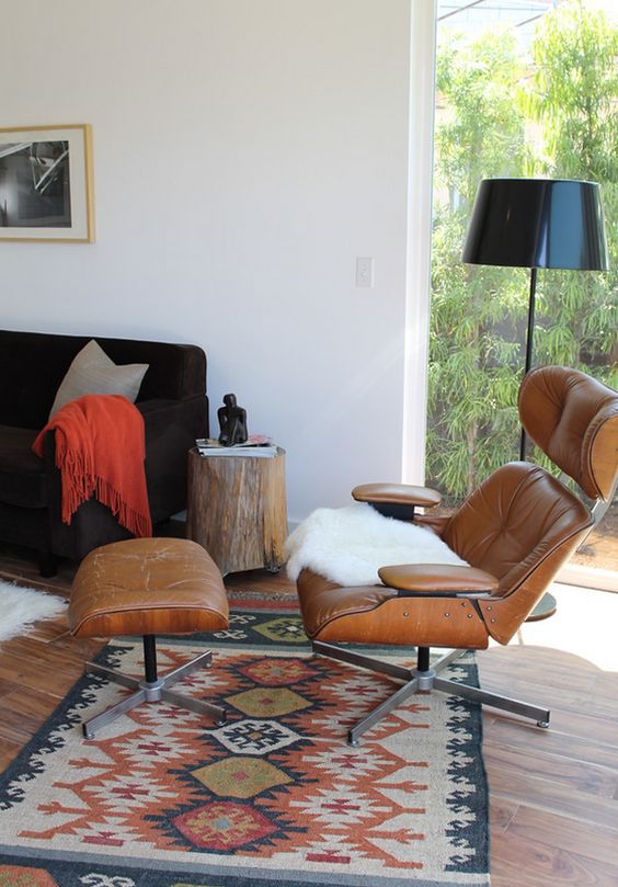 a mid century modern living room with a black sofa, an amber leather chair with an ottoman, a black floor lamp and a bold rug