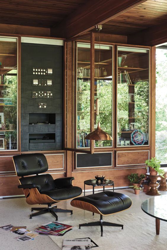 a mid-century modern living room with a built-in glazed storage unit, a black Eames lounger, a glass coffee table and potted plants