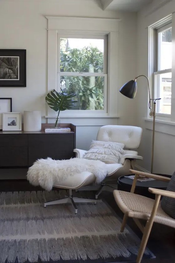 a mid-century modern living room with a dark-stained credenza, a white Eames lounger and ottoman, a rattan chair, a black side table