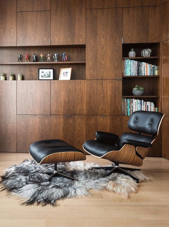 a mid-century modern space with a large storage unit that takes a whole wall, a black Eames lounger and a faux fur rug