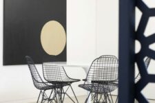 a minimal dining space with a white round table, black Eames wire chairs, a statement artwork and nothing else