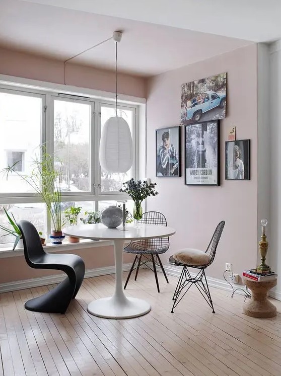 a modern dining space with pink walls, a gallery wall, white table, a sculptural chair and Eames wire chairs, a pendant lamp and some decor