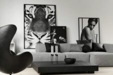a monochromatic living room with a grey low sofa, a black coffee table, a black Egg chair and some black and white artwork