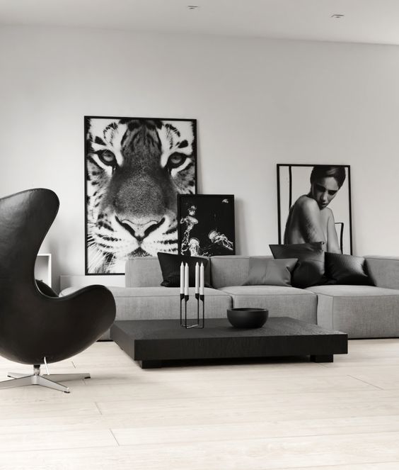 a monochromatic living room with a grey low sofa, a black coffee table, a black Egg chair and some black and white artwork