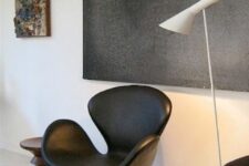 a monochromatic space with an oversized artwork, a black leather Swan chair, a white floor lamp and a stack of black pillows