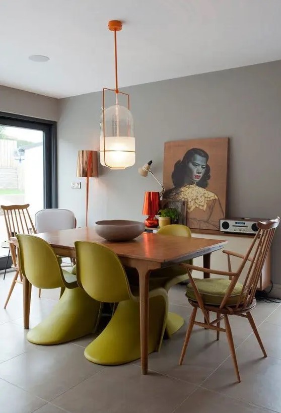 a moody dining room with grey walls, a stained table and mustard Panton chairs, some stained ones, a credenza and a bold artwork