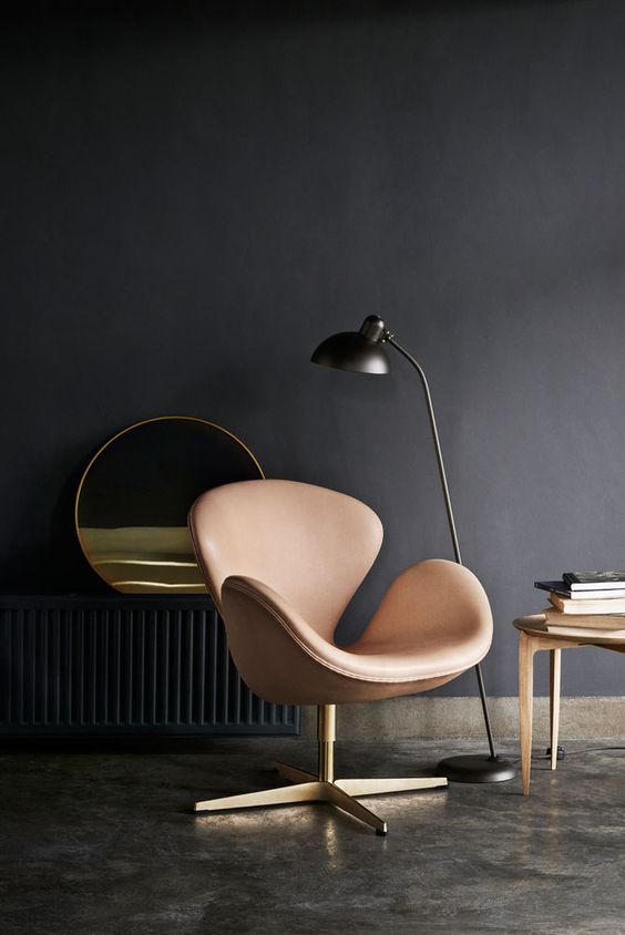 a moody living room with a blush Swan chair, a black floor lamp, a side table and a round mirror is catchy