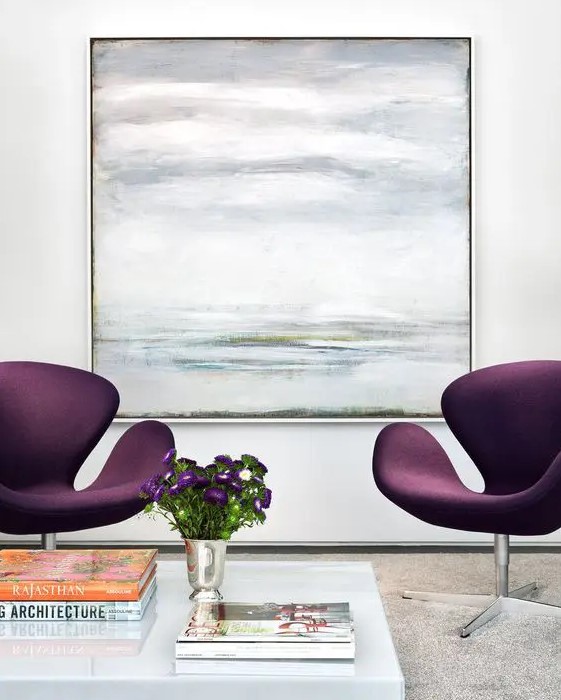 a neutral living room with an artwork, purple Swan chairs, a low coffee table with magazines and blooms