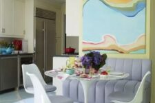a pastel dining space with an oversized artwork, a lilac sofa, an oval table and lilac Tulips and bold blooms is a chic idea