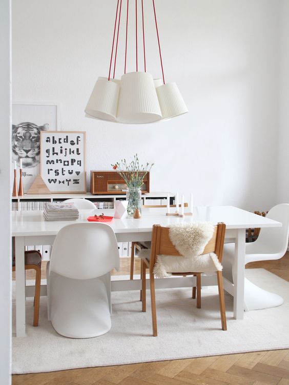 a pretty Scandinavian dining space with a white table, white chairs including Panton, a cluster of pendant lamps and a credenza with art