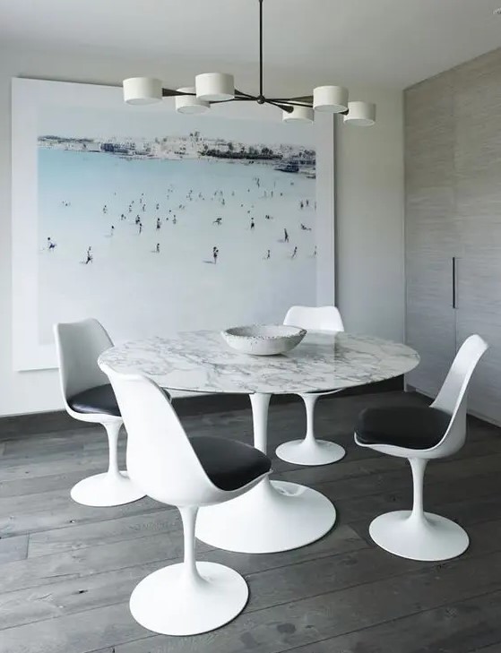 a pretty dining space with an oversized artwork, a round table, black and white Tulip chairs and a cool chandelier