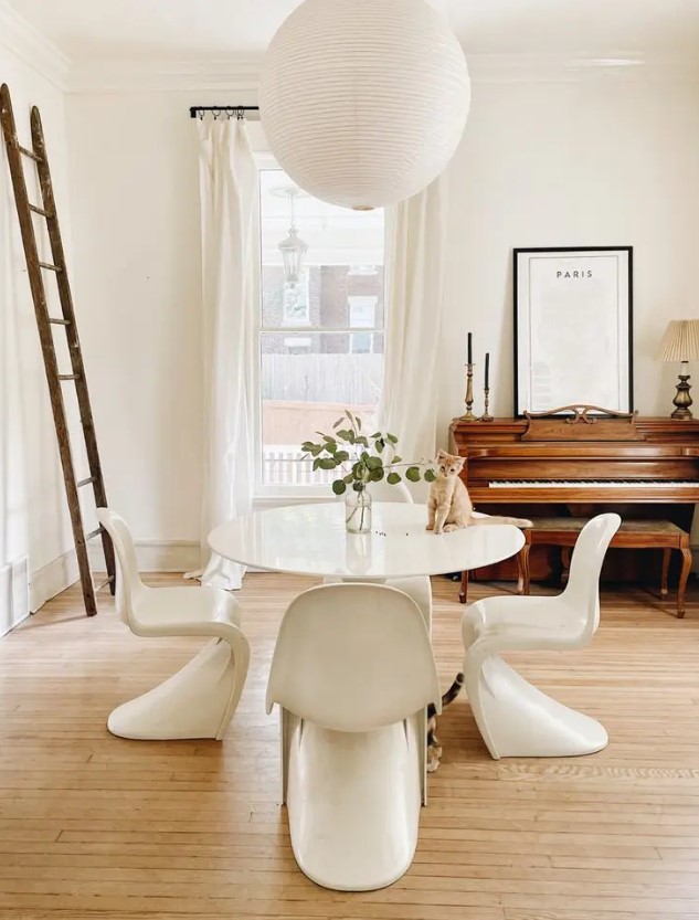 a refined Parisian dining room with a vintage paino and a stool, a white table and Panton chairs, a ladder and a pendant lamp