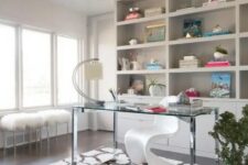 a refined home office with built-in storage units and shelves, a clear glass desk, a white Panton chair and faux fur stools