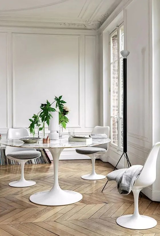 a refined neutral dining space with a Parisian feel, with stucco, a roudn table, grey Tulip chairs and stacks of vinyl
