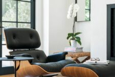 a refined space with a black Eames lounger, a woven stool with an orchid, a small black side table and glazed doors