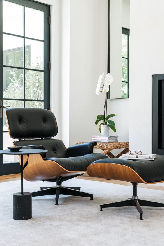 a refined space with a black Eames lounger, a woven stool with an orchid, a small black side table and glazed doors