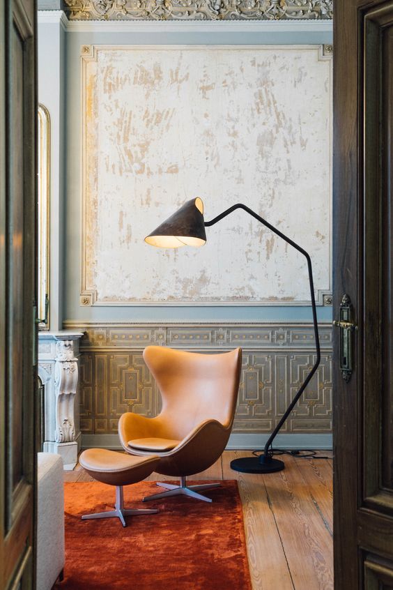 a refined vintage space with molding and touches of gold, an amber Egg chair and an ottoman and a floor lamp