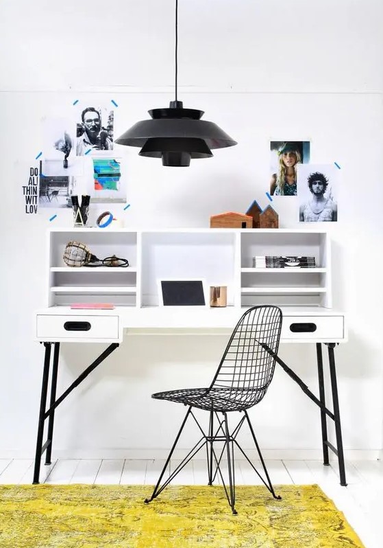 a small and catchy working space with a black and white desk, a black Eames chair, a black pendant lamp and some photos for inspiration