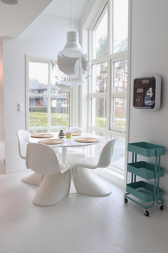 a small dining space by the window with a white table, white Panton chairs, a pendant lamp and a lot of light