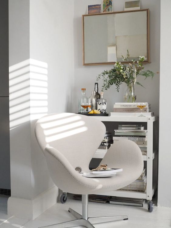 a small neutral nook with a mirror in a gold frame, a creamy Swan chair, a neutral storage unit on casters and greenery