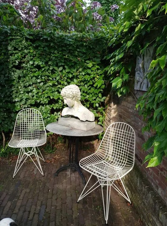 a small outdoor space with a living wall, a round table with decor and a couple of Eames wire chairs in white