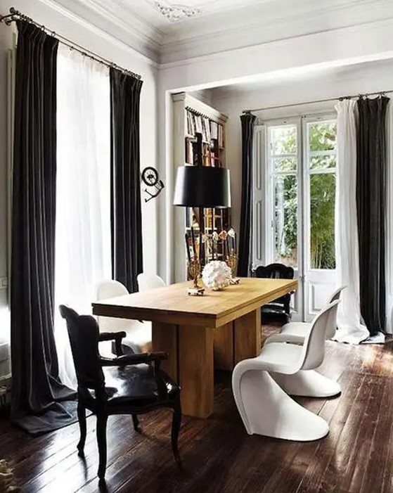a sophisticated dining room with a bookcase, a stained table, black vintage and white Panton chairs, black curtains and a lamp