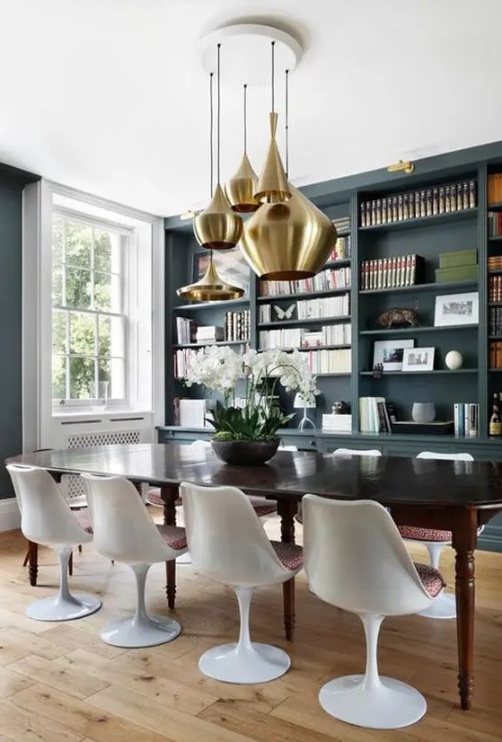 a sophisticated dining room with slate grey walls, a large built in storage unit, a black dining table and Tulip chairs plus a cluster of brass pendant lamps