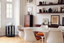 a sophisticated dining space with an oval table, rust-colored chairs, stained shelves, a credenza, a cabinet and some decor and art