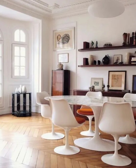 a sophisticated dining space with an oval table, rust colored chairs, stained shelves, a credenza, a cabinet and some decor and art