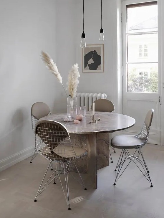 a stylish Scandinavian dining space with a round stone table, Eames wire chairs with seat pads, pendant bulbs and some decor