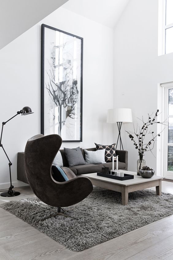 a stylish Scandinavian living room with a taupe sofa and bold pillows, a brown Egg chair, a low coffee table and some lamps plus an artwork
