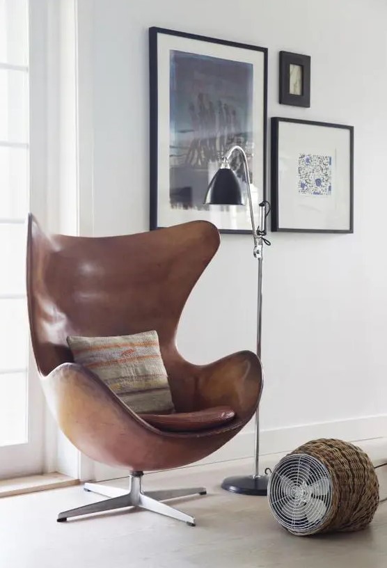 a stylish and catchy nook with a mini gallery wall, a brown leather Egg chair, a floor fan and a black floor lamp