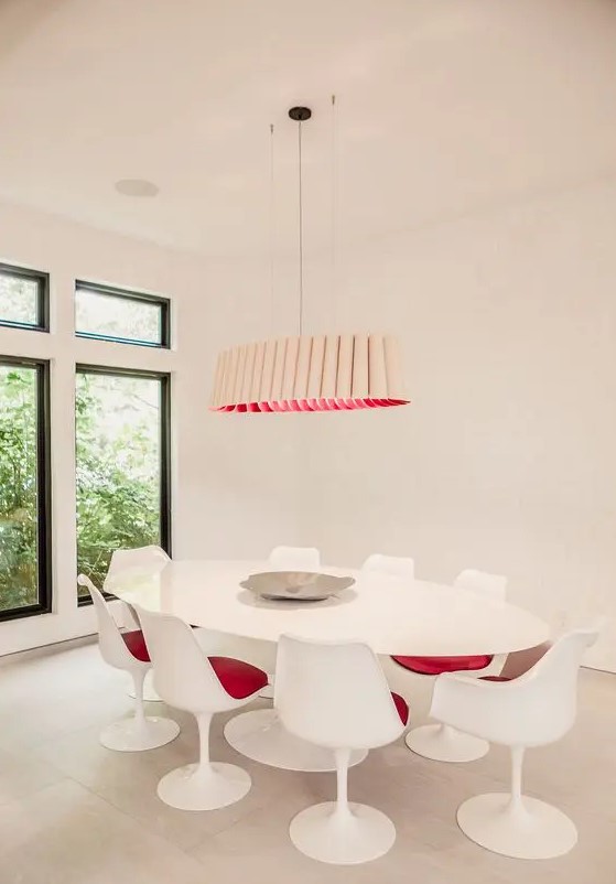 a stylish modern dining space in creamy shades, with a large oval table, pink Tulip chairs, a catchy tube-like chandelier with pink inside