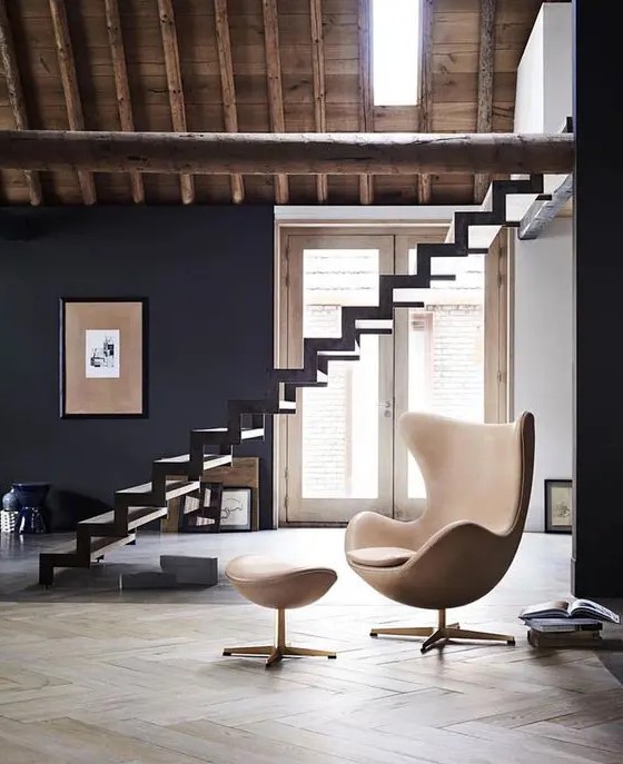 a stylish space with a black wall, a skylight, a black ladder, a beige Egg chair with a footrest is chic