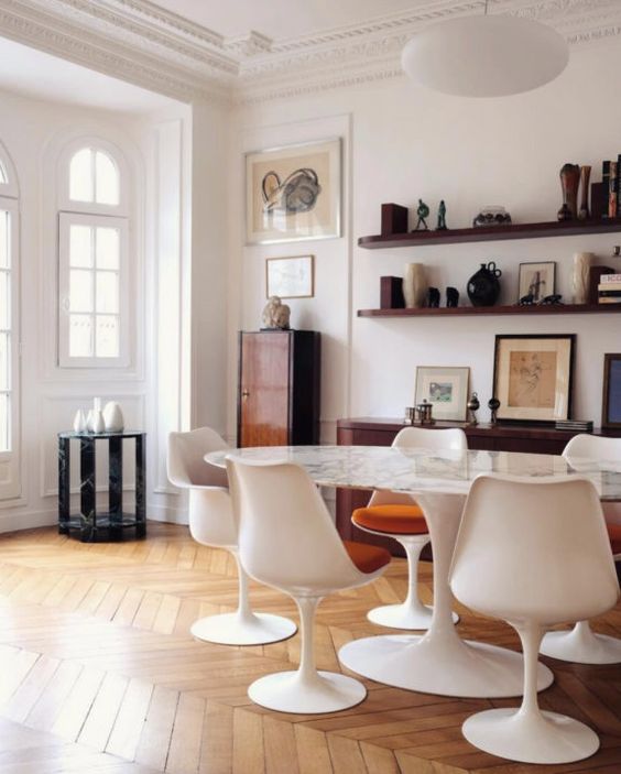 a vintage dining space with open shelves, an oval table, white Tulip chairs, some beautiful and sophisticated decor