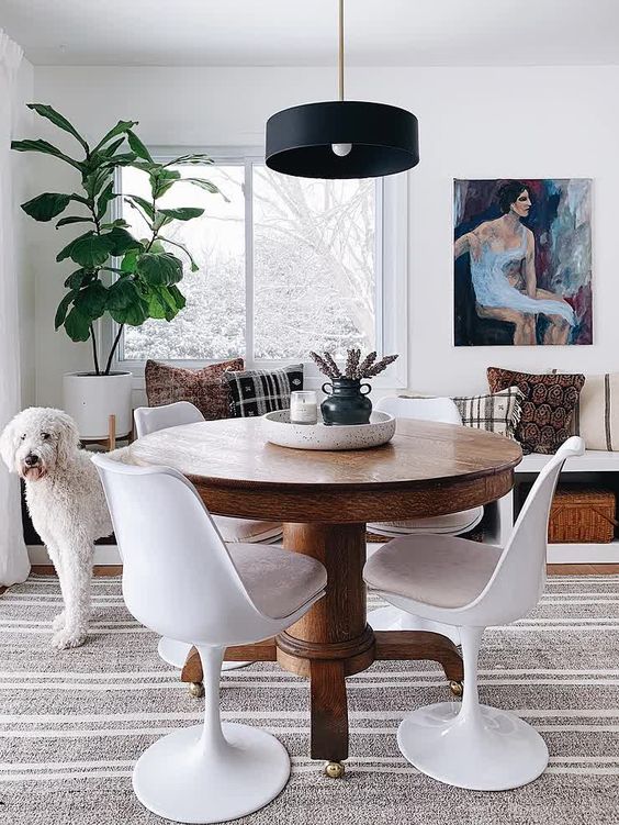 a welcoming dining room with a windowsill bench, a stained vintage table, neutral Tulip chairs, a black pendant lamp