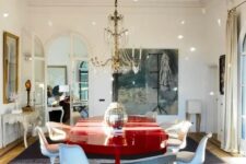 a whimsical dining room with an oversized artwork, a red dining table, neutral Tulip chairs and a metal one, a chic chandelier and a disco ball centerpiece