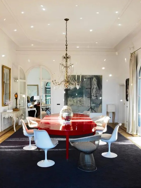 a whimsical dining room with an oversized artwork, a red dining table, neutral Tulip chairs and a metal one, a chic chandelier and a disco ball centerpiece