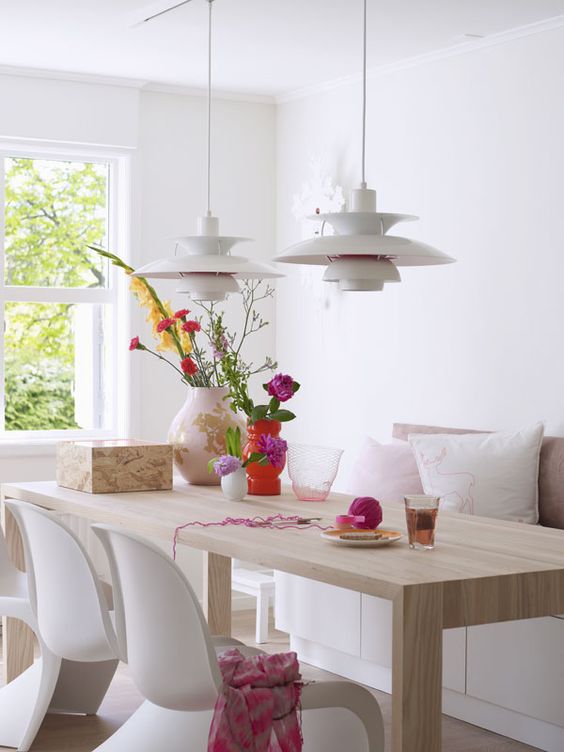 an airy dining space with a storage bench, a stained table, white Panton chairs, white pendant lamps and bold decor