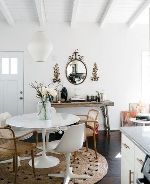 an eclectic dining room with a round table, mismatching chairs including Tulip ones, a jute rug, a wooden console table
