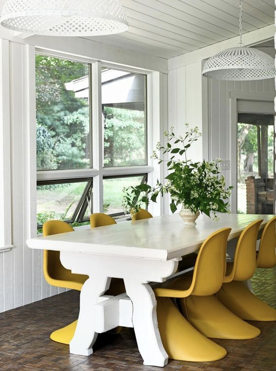 an eclectic dining space with a large white table, yellow Panton chairs, greenery and blooms is a cool and lovely space