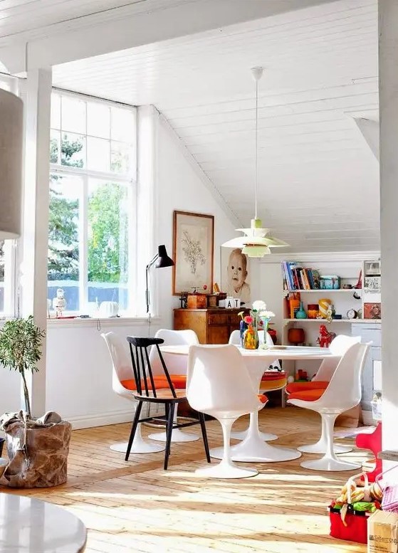 an eclectic dining space with open shelves with books, a vintage sideboard, a round table and orange Tulip chairs, a pendant lamp and a black table one