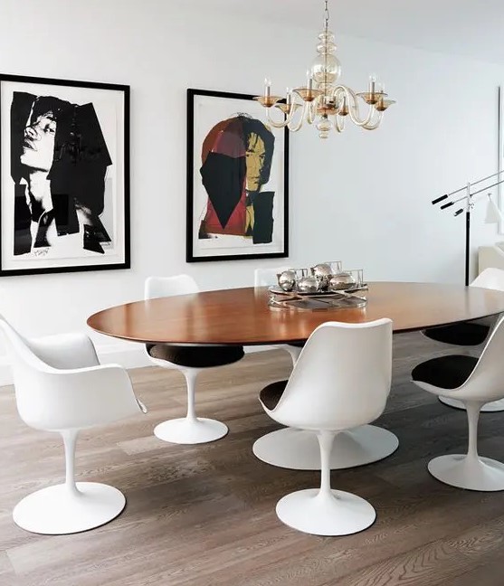 an elegant dining room with an oval table and black and white Tulip chairs, a mini gallery wall and a gilded chandelier