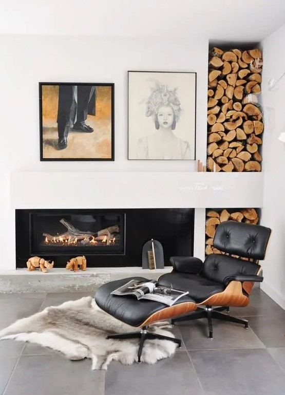 an elegant fireplace nook with a built in fireplace, a black Eames lounger and an ottoman, a rug, a firewood storage niche