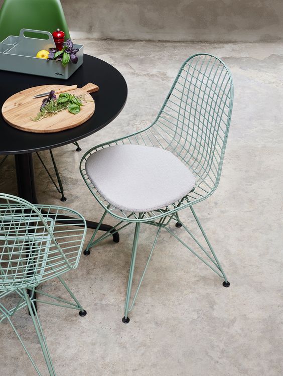 an outdoor dining space with a black table, green Eames wire chairs with and without cushions and some decor