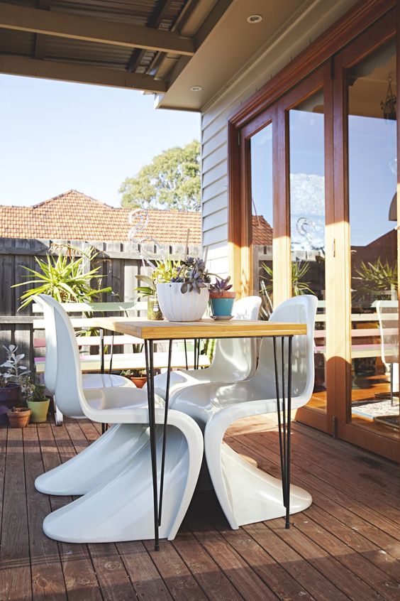 an outdoor dining space with a hairpin leg table, white Panton chairs and some potted plants is a cool space