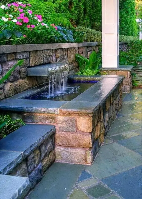 a beautiful waterfall with a large water feature in stone and brick and surrounded with greenery and bold blooms is a cool idea