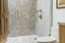 04 a catchy and light-filled neutral bathroom clad with neutral Zellige tiles, a skylight over the shower, white appliances and gold fixtures