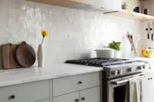 a chic dove grey kitchen with a white zellige tile backsplash, light-stained shelves and white stone countertops is amazing
